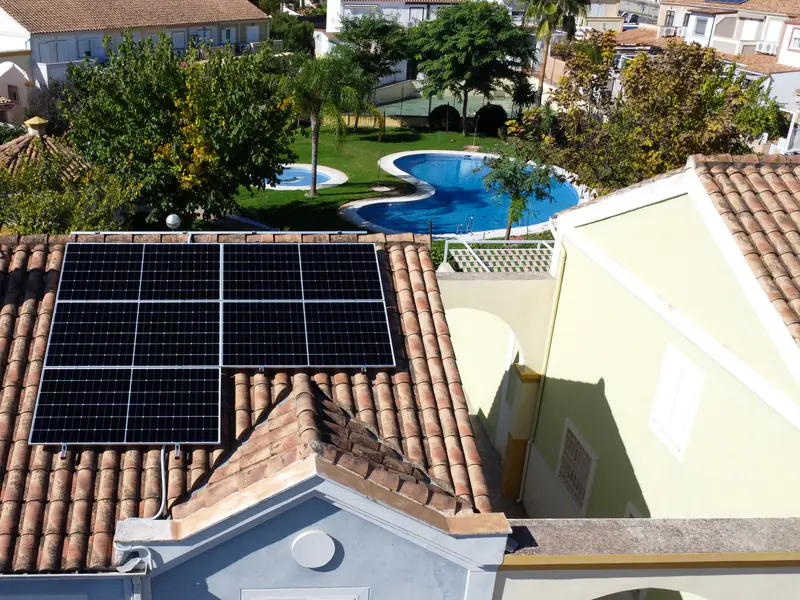 Placas solares instaladas por Efitea sobre un tejado de teja, con piscina comunitaria al fondo